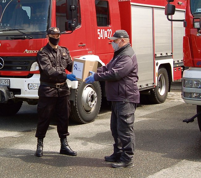 Dyrektor Zakładu Karnego w Strzelinie Robert Stasz (z prawej) przekazuje 200 maseczek na ręce Michała Pięty, komendanta Komendy Powiatowej Państwowej Straży Pożarnej w Strzelinie